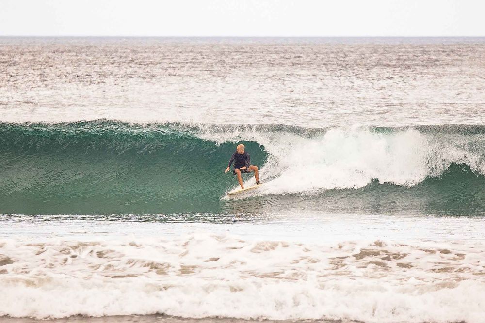 A surfer rides a green wave in the ocean during an overcast day.