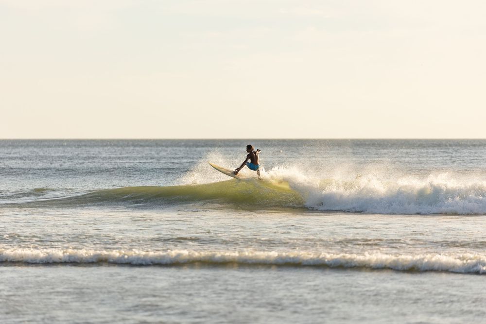 A surfer rides a wave during golden hour at the beach as the sun sets over the ocean.