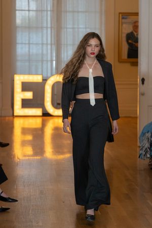 Models walk the runway in black evening wear collection at a fashion show with illuminated backdrop.