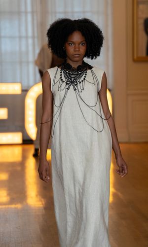 Model showcases flowing white dress with collar detail on illuminated runway.