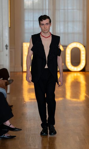 Model in all-black ensemble walks down illuminated runway with glowing ECO sign in background.