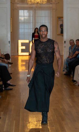 Model showcases sleek black ensemble with flowing skirt on runway with illuminated ECO sign in background.
