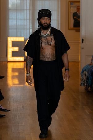 A person in black clothing walks down a wooden hallway with illuminated walls and warm lighting.