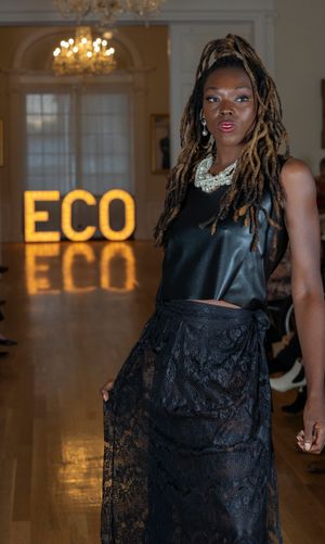 Model presents black lace evening gown during fashion show with ECO branding visible.