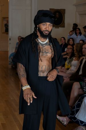 Model in black attire strikes dynamic poses on runway during fashion show with audience in background.