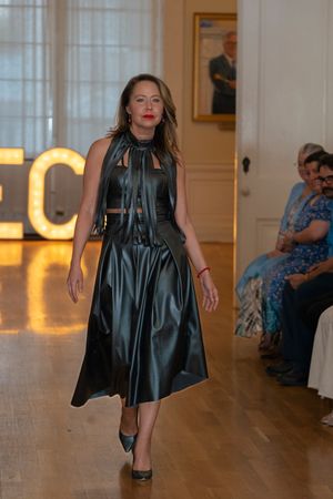 Model showcases flowing black dress on catwalk with illuminated ECO signage.