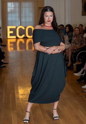 Plus size fashion model struts down catwalk in elegant black ensemble during runway show.