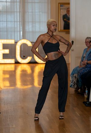 Fashion model walks runway in black outfit with dramatic pose sequence showing movement on wooden floor.