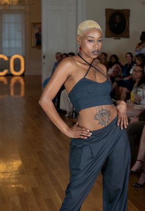 Model in dark athletic wear performs dynamic dance movements on wooden stage with illuminated ECO sign in background.