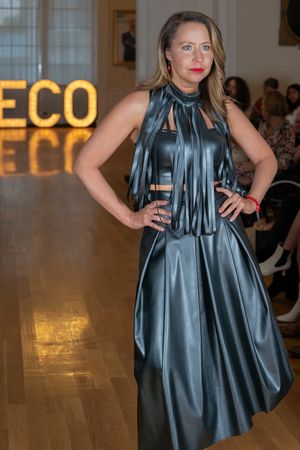 Fashion model wearing metallic gray dress with fringe details walks runway at fashion show.