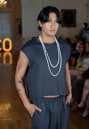 Model showcases sleek black crop top with pearl necklace on fashion runway with ECO signage.