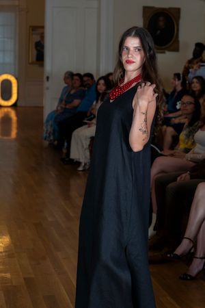 Fashion model walks runway in elegant black blazer with dramatic red lipstick at indoor fashion show.