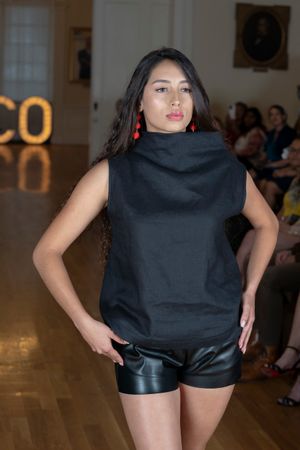 Fashion model showcases black top and leather shorts on wooden runway.