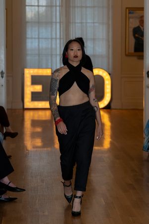 Performer in black outfit executes dance moves on hardwood floor with glowing ECO letters in background.