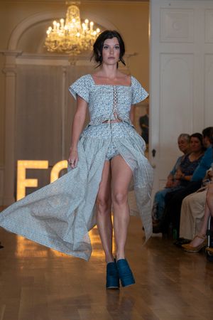 Model presents white eyelet dress with boots during fashion show performance.
