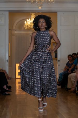 Model twirls in black and white patterned dress on elegant runway with chandeliers.