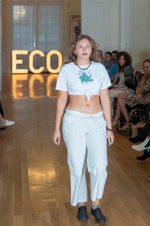 Model walks runway in all-white ensemble featuring cropped t-shirt and loose pants at fashion show.