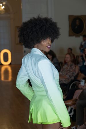 Model presents white-to-green ombre jacket on fashion runway with glowing ECO signage behind.