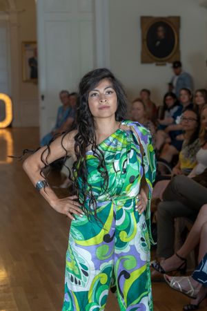 Model showcases vibrant green and white patterned dress on indoor catwalk.