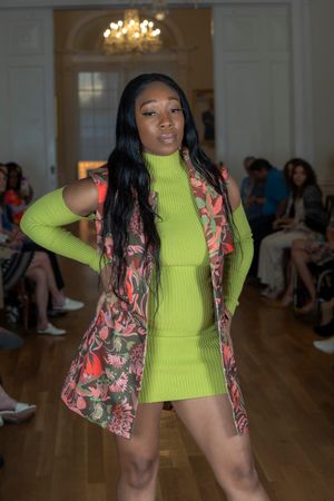Model struts down runway in neon green top and floral print vest.