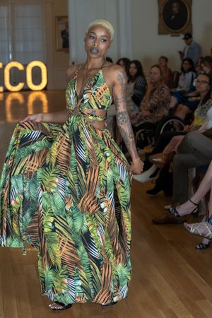 Model showcases tropical print dress with palm leaf pattern on fashion runway.