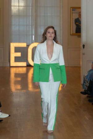 Model displays color-block white and green pantsuit while walking down wooden runway.