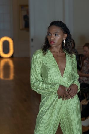 Model walks runway in lime green textured jumpsuit with plunging neckline and long sleeves during fashion show.