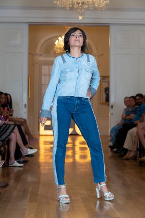 Model presents denim-on-denim look with light wash shirt and dark jeans on wooden runway.