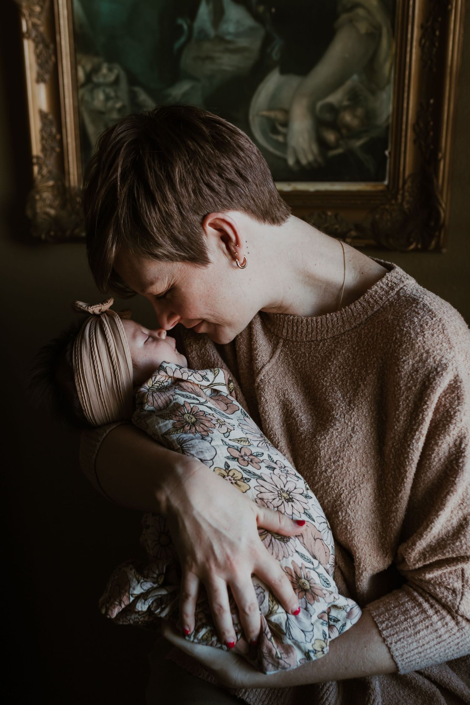 Mother tenderly touching noses with her newborn baby wrapped in a floral blanket indoors.