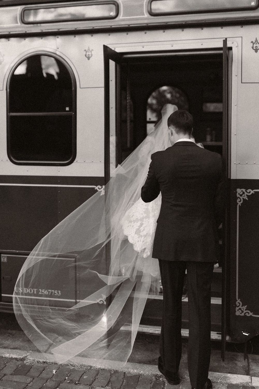 A wedding couple poses near a vintage train car with the bride's veil flowing in the wind.