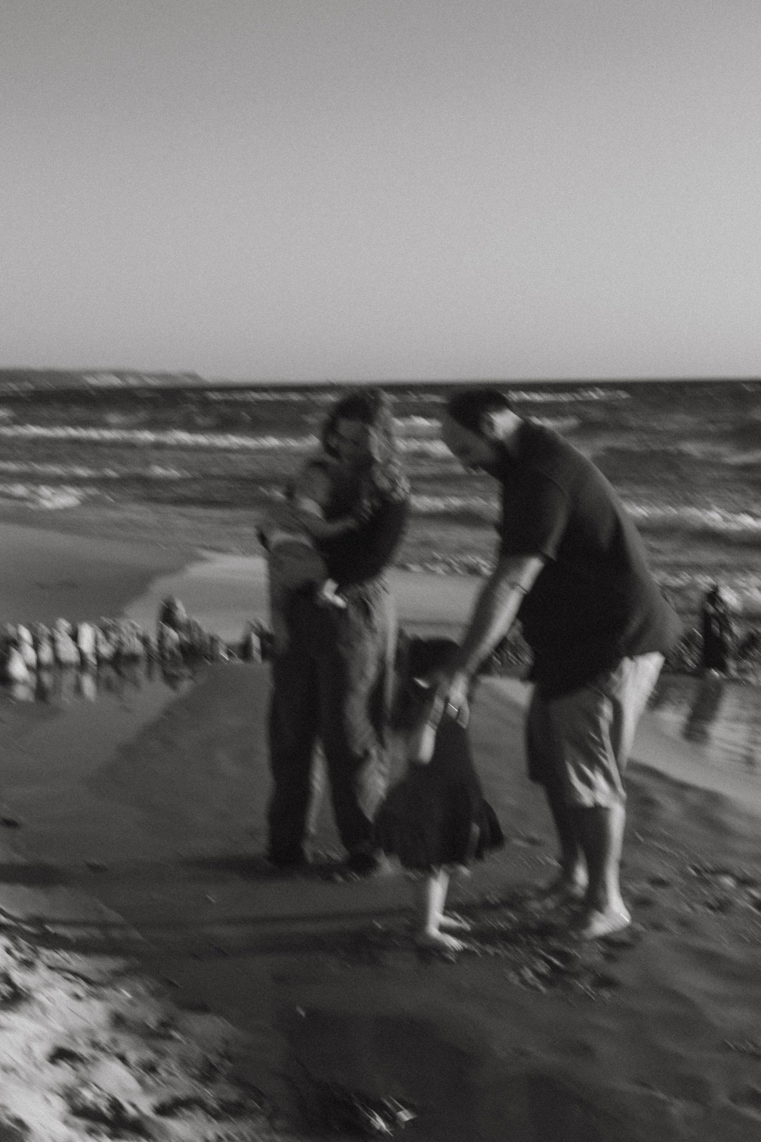 Black and white photo of family playing together on sandy beach near ocean waves.