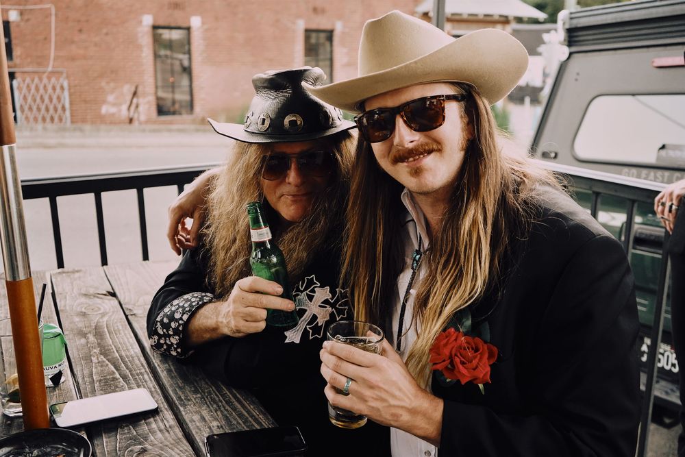 Casual gathering of people with cowboy hats enjoying drinks at an outdoor table.