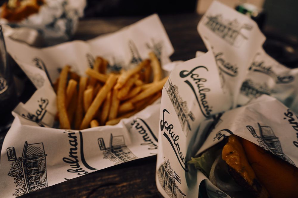 Fresh french fries served in branded paper wrappers at an outdoor dining establishment.