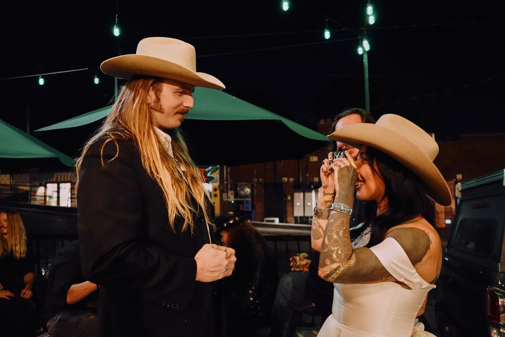 Nighttime gathering with green lighting and cowboy hats creating an atmospheric western ambiance. Romantic photo of bride taking film photo