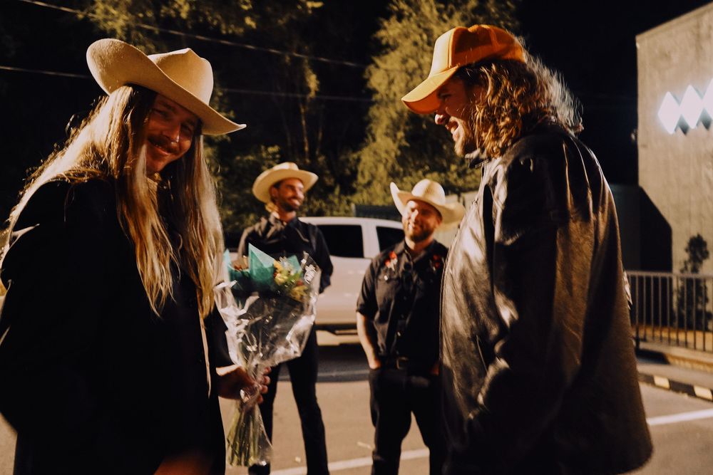 Nighttime social gathering with wedding guests wearing western attire under outdoor lighting.