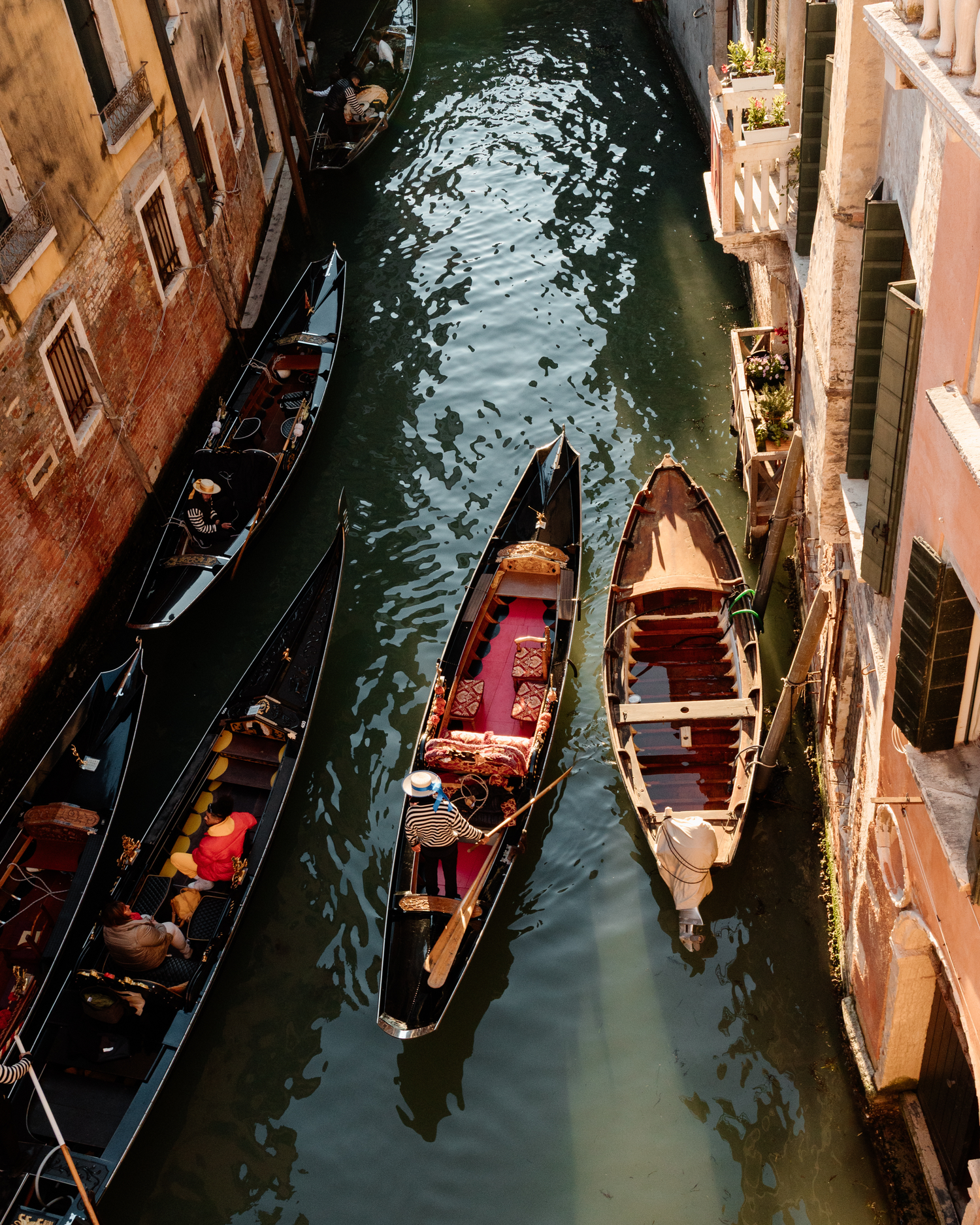 Aerial view of traditional Venetian gondolas navigating through narrow canals between historic buildings.