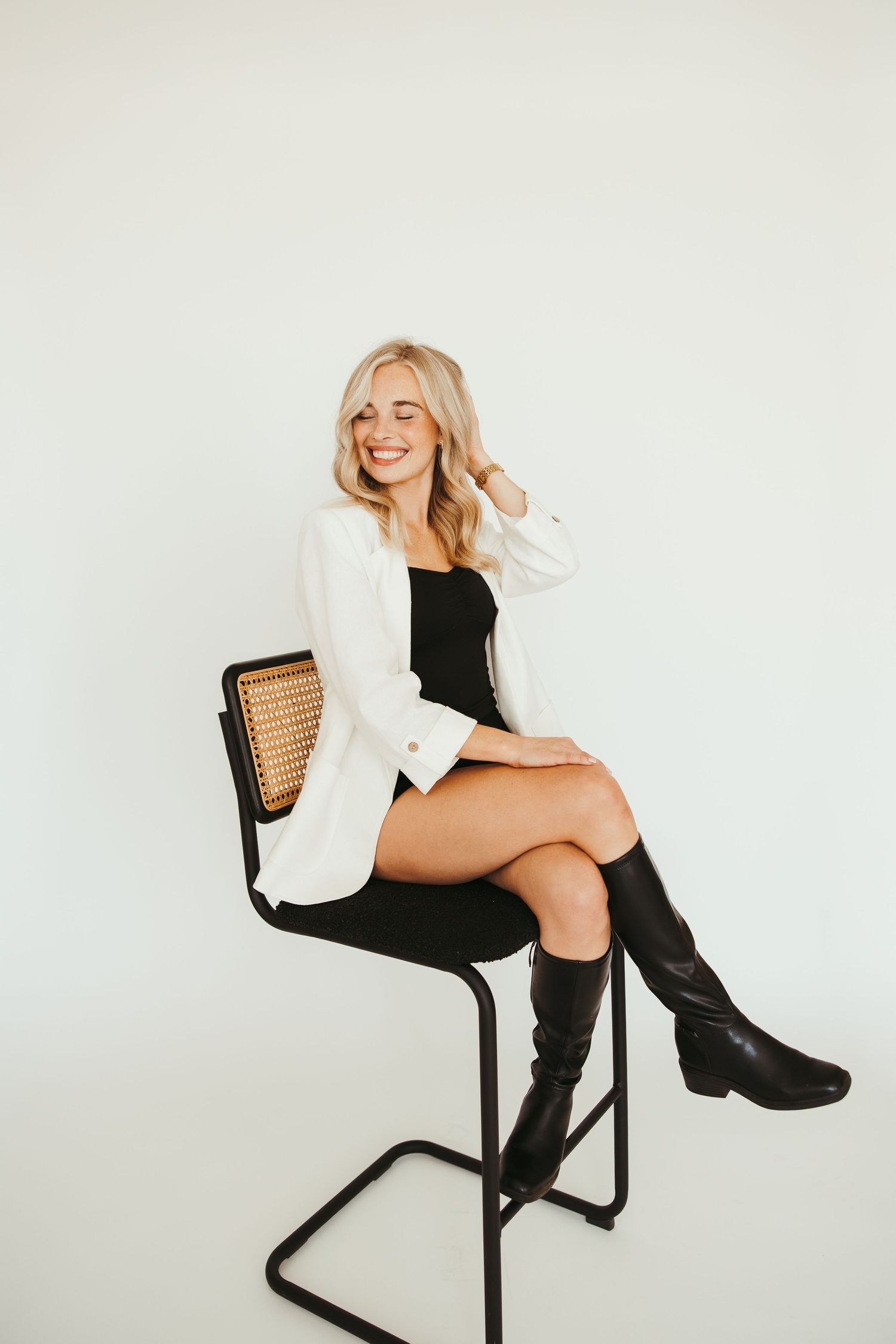 Smiling blonde woman in white sleeveless top posing against white wall.