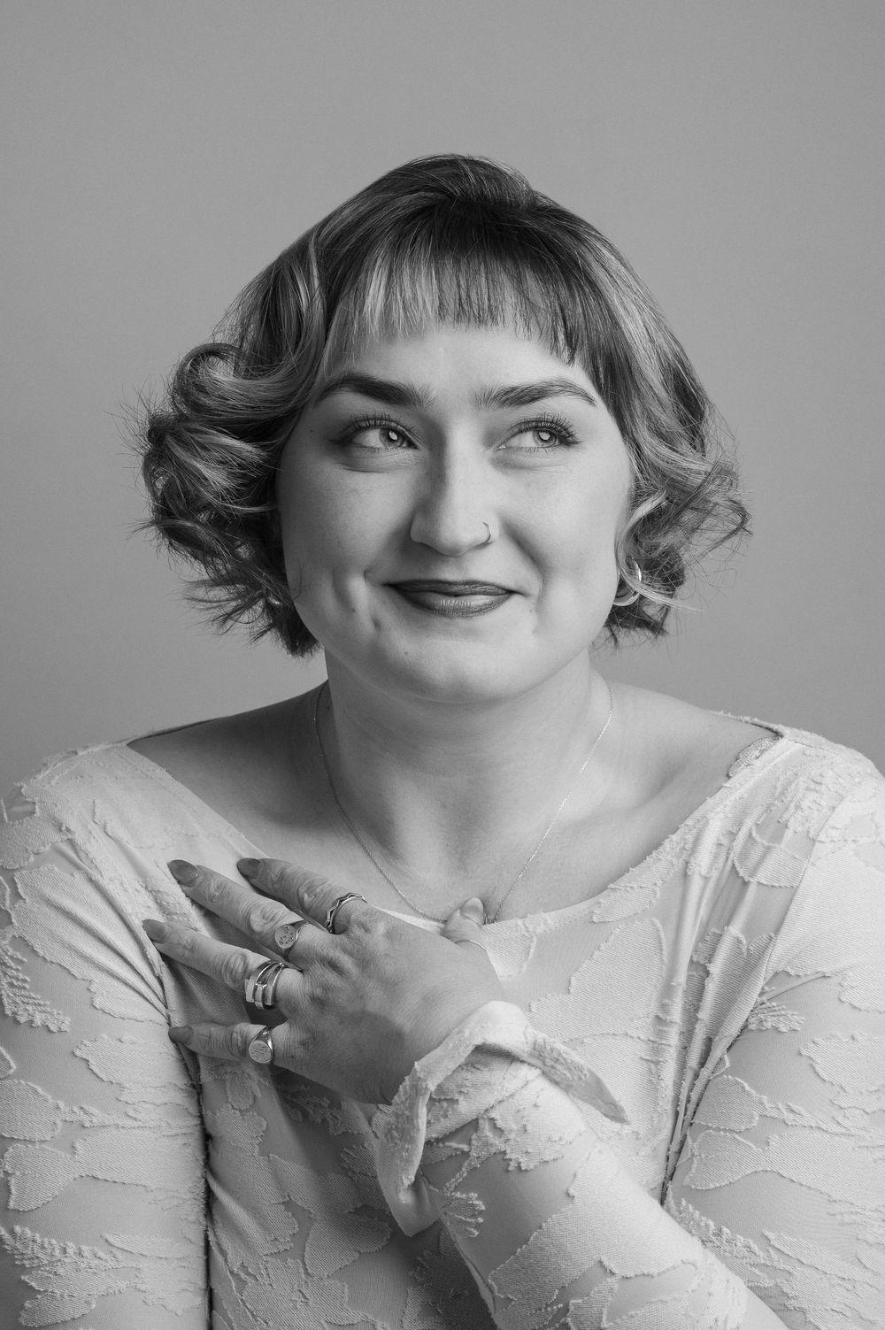 A series of black and white portraits showing playful expressions and poses while wearing a white lace top.