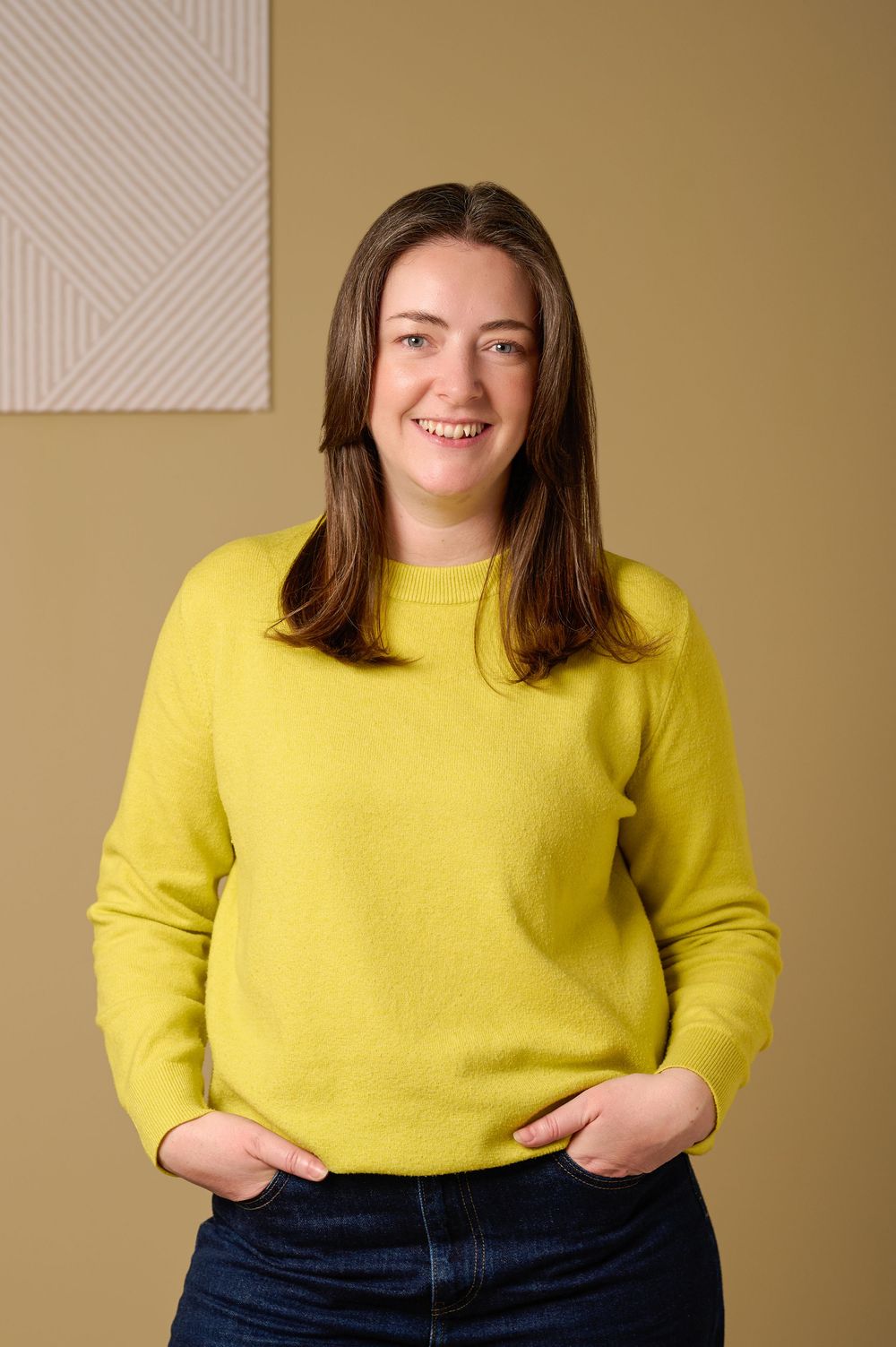 Person wearing a bright yellow sweater and dark jeans poses against a beige background in a casual portrait series.