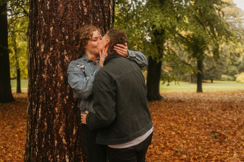 A couple shares a tender moment against a large tree trunk with autumn colors in the background.