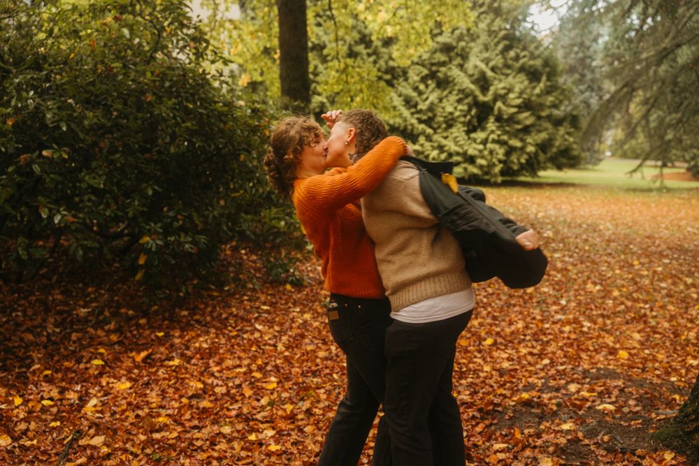 Autumn scene with orange sweater and fallen leaves in a park setting with golden foliage.