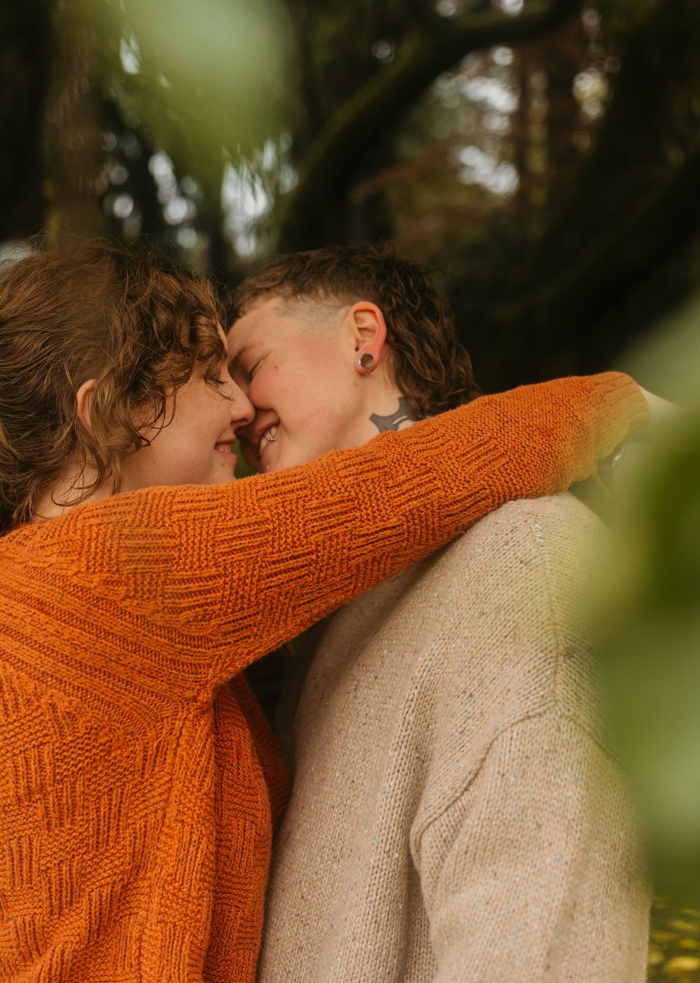 A romantic autumn scene with two people embracing while wearing cozy sweaters in warm fall colors.