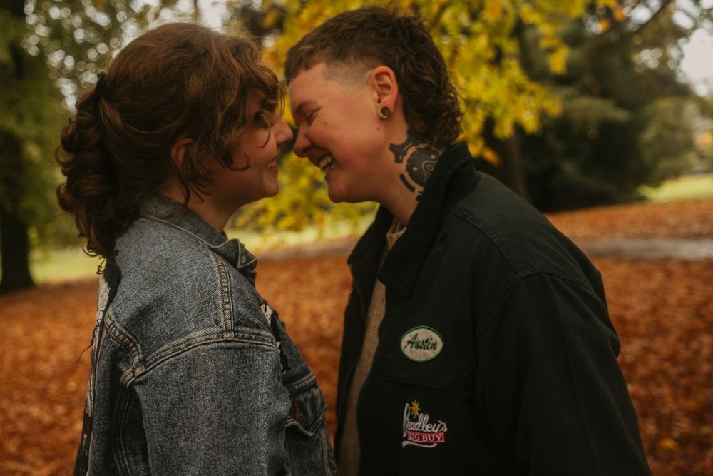 A couple shares an intimate moment surrounded by autumn leaves in a romantic outdoor setting.