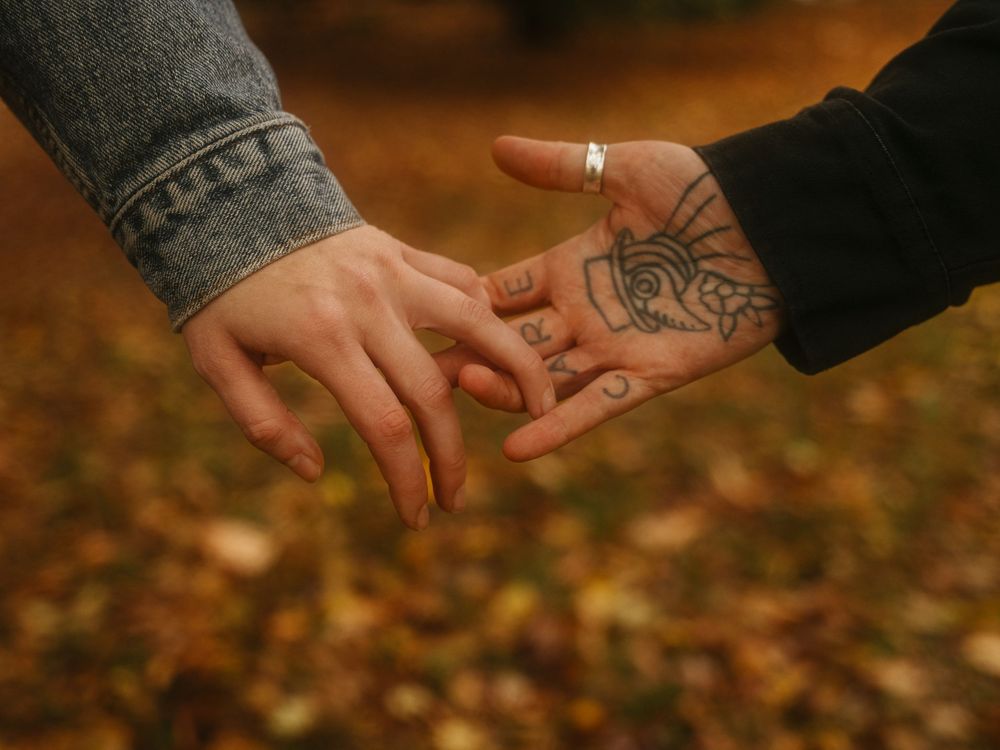 Hands reaching across autumn leaves in warm lighting creating a romantic connection.