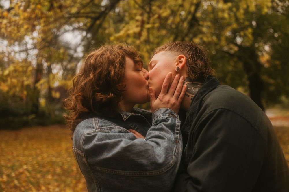 A romantic couple embraces surrounded by golden autumn foliage in a park setting.