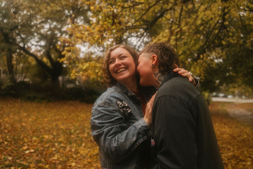 A couple shares a joyful moment together surrounded by golden autumn foliage in a park setting.
