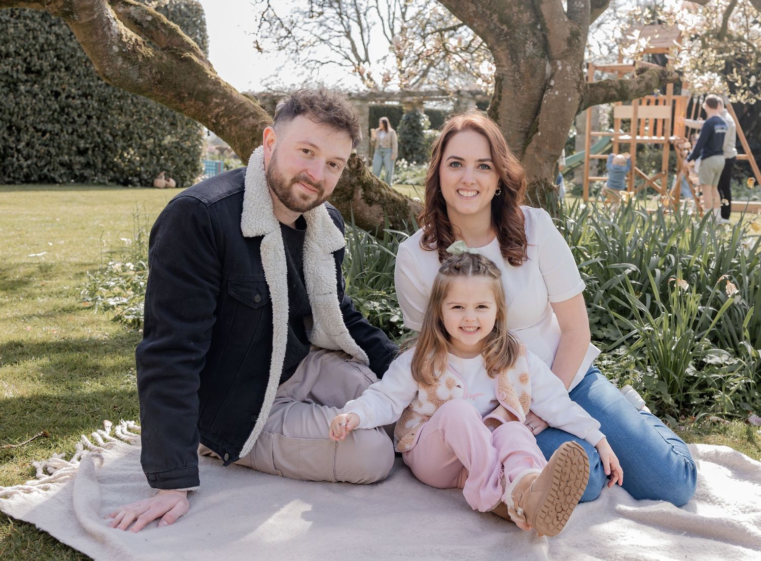 Family wearing festive sweaters posing together by Christmas tree. Photography in Buckinghamshire.