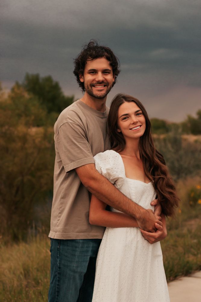 A couple embraces outdoors during golden hour in a desert landscape wearing casual clothes .|Westminster Colorado Family Photographer