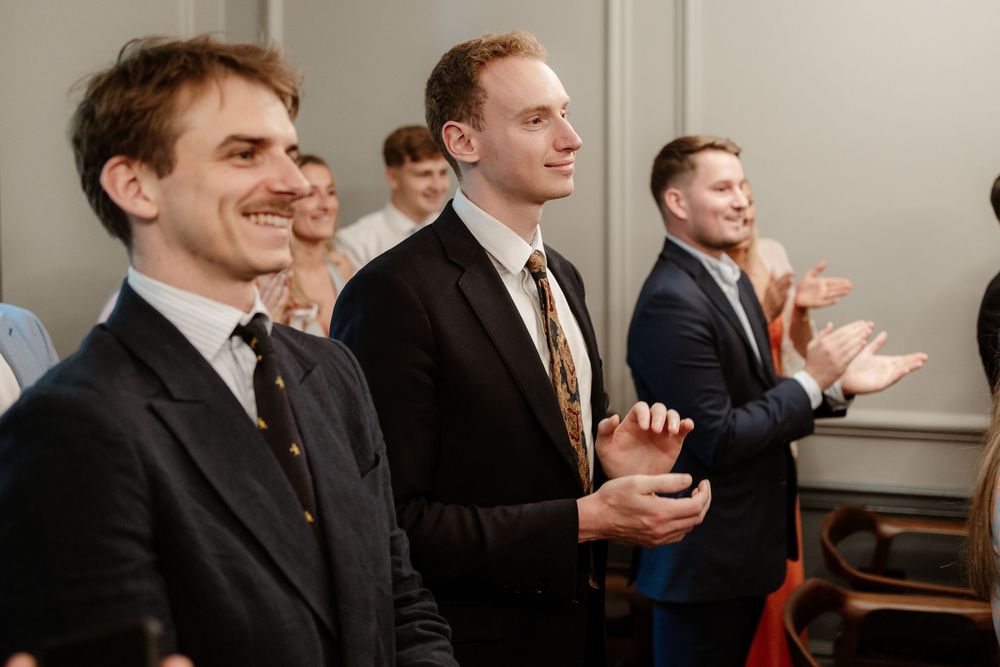 Business people in suits sit together at a conference table laughing and smiling during a meeting.
