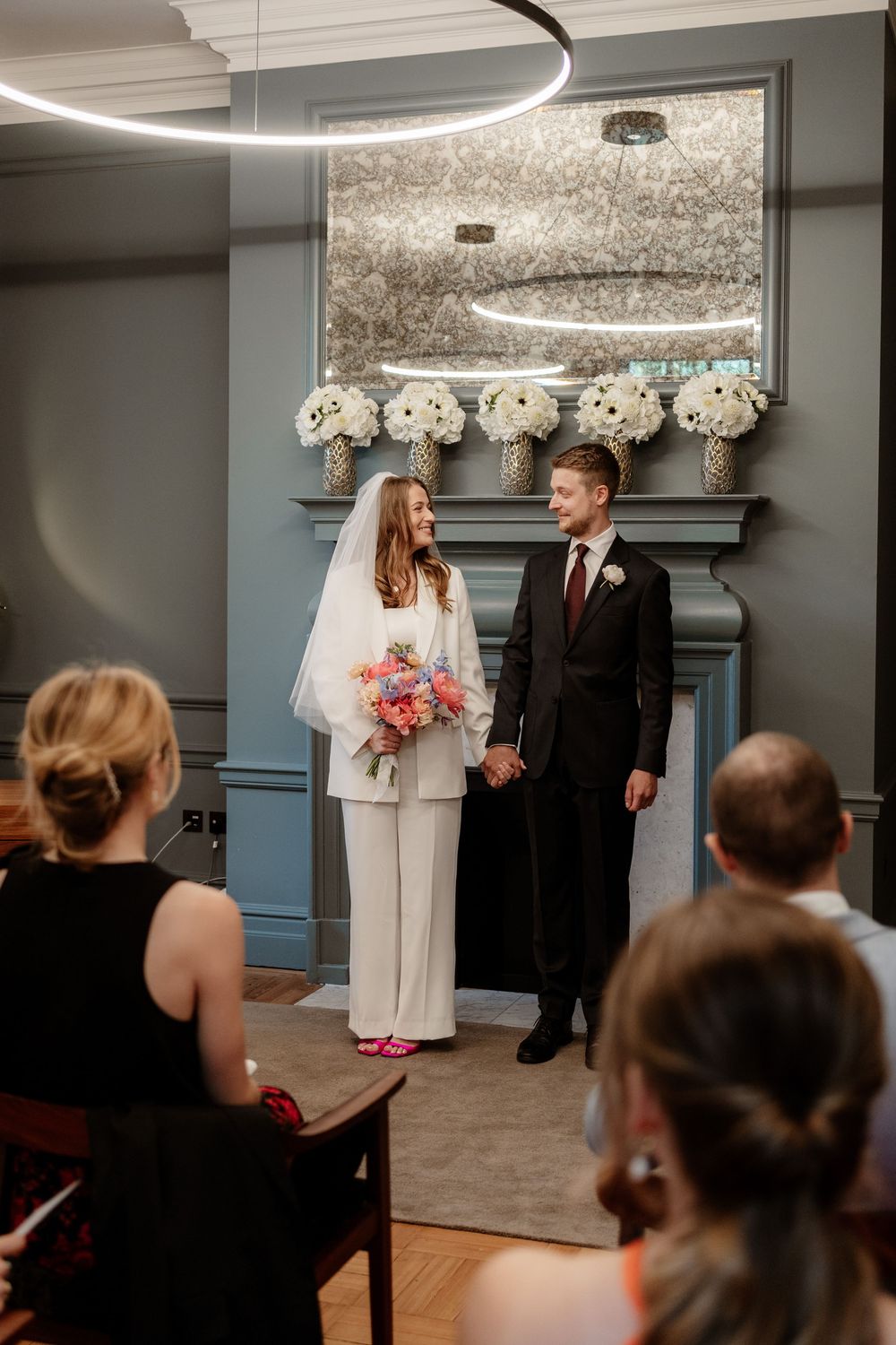 A wedding ceremony taking place in a modern room with circular lighting and grey walls.